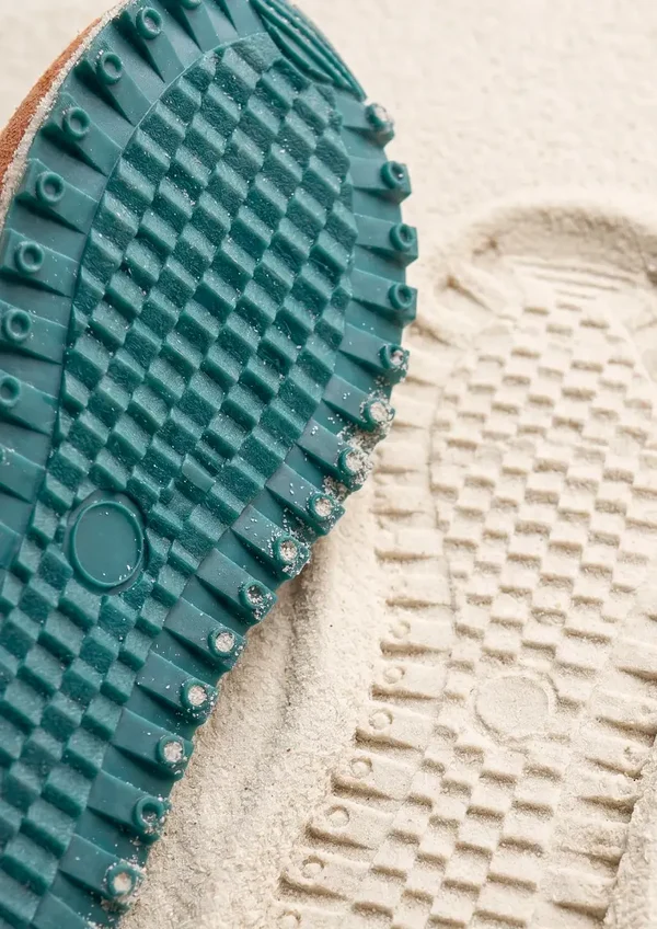 Close-up of the Novera shoe outsole tread pressed into sand